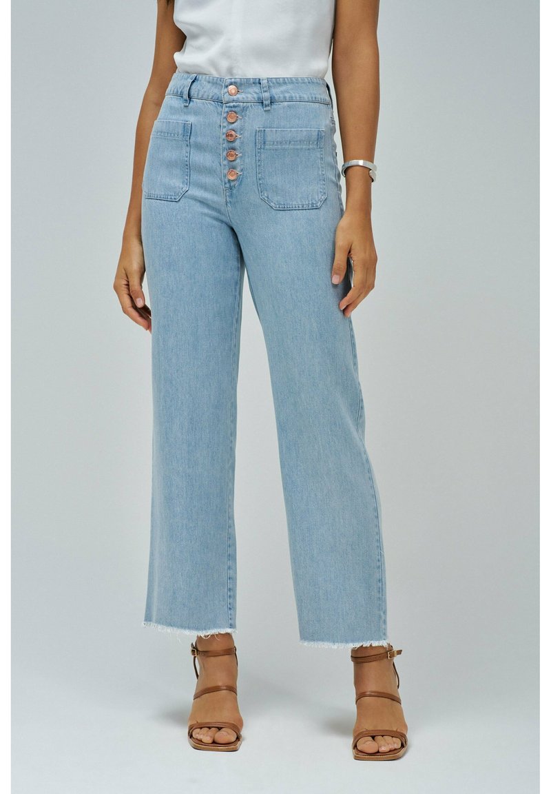 Svetlo modre visokorasle kavbojke z ravnim nogavicom, surovim robom in petimi bakrenimi gumbi spredaj. Vidni sta dve sprednji žepi.