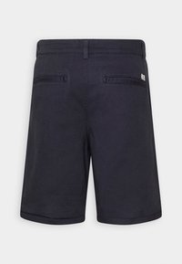 Marinblå skräddarsydda shorts med bältesöglor och två bakfickor i västformat, uppvisade mot en ljus, enfärgad bakgrund.