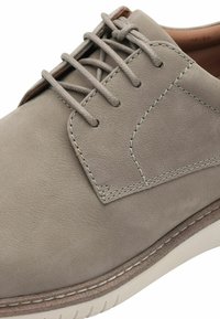 Scarpa in pelle grigia chiara con una texture liscia, punta tonda e suola beige. Presenta cuciture decorative e un design classico con lacci.