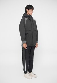 Grå huva jacka med kontrasterande mörkare ärmar och stora framfickor, kombinerad med svarta joggers med vita sidostrickar och vita sneakers.