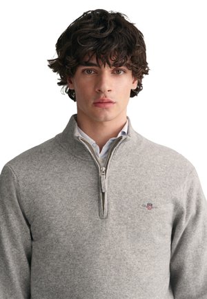 Grauer Reißverschluss-Pullover aus weichem Stoff, mit einem gerippten Kragen und kleinem gesticktem Logo auf der Brust. Glatte Textur, lange Ärmel.