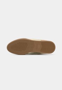 Light beige sneaker sole with a textured, wavy pattern; features a durable rubber material. Logo embossed in the mid-sole area.