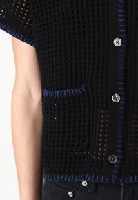 Black knitted cardigan with a loose weave, blue accents along the edges and pocket, and silver buttons. Features a single front pocket.