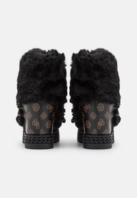 Une paire de bottines noires avec une tige en fausse fourrure, un talon en cuir à motifs et une semelle texturée, vues de l'arrière sur un fond blanc.