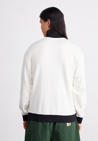 Witte sweatshirt met een zwarte kraag en geribbelde manchetten, met een relaxte pasvorm en zachte textuur. Draag met groene shorts, met een achteraanzicht.