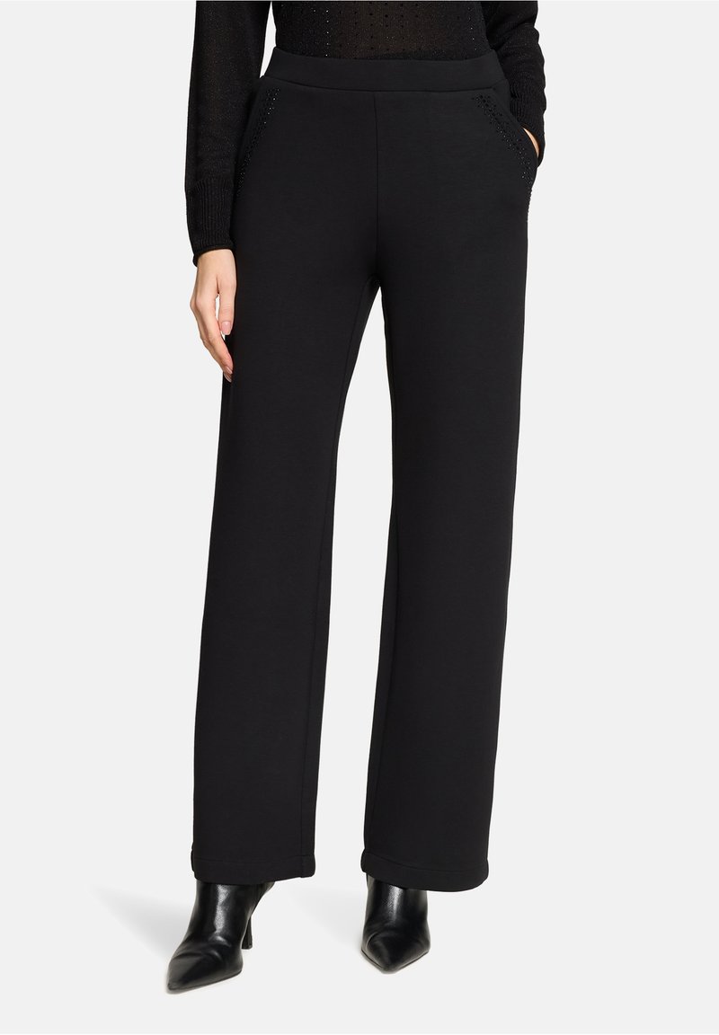 Czarne spodnie dresowe o gładkiej fakturze, szerokim kroju nogawek i bocznych kieszeniach. Posiadają subtelne zdobienia w okolicach kieszeni.