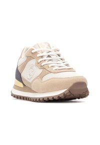 Zapatilla deportiva beige y blanca con materiales de ante y malla, forma redondeada, suela texturizada y detalle del logo en el lateral.