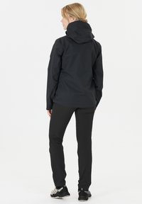 Zwarte waterdichte jas met een capuchon, gecombineerd met zwarte broeken en wandelschoenen. De jas heeft een gladde, gestructureerde afwerking.