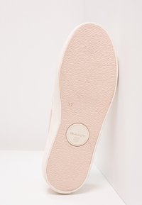 Semelle d'une sneaker rose avec une texture antidérapante, logo GANT, et numéro de taille 37 visible, inclinée contre un fond de coin blanc.