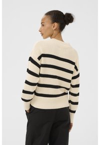 Knit sweater in cream with black horizontal stripes, featuring a ribbed crew neck and loose fit. Visible seams and textured knit pattern.