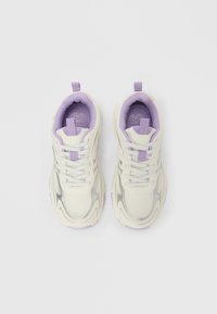 Crème- en zilverkleurige sneakers met veters, lila voering aan de binnenkant en trekbandjes, gezien van bovenaf op een effen witte achtergrond.