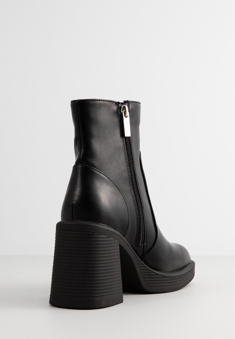 Bottines noires avec un talon en caoutchouc texturé, fermeture éclair sur le côté, finition en cuir lisse et design à bout rond.