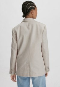 Beige maßgeschneiderter Blazer mit Reverskragen, Ein-Knopf-Manschetten und strukturierte Schulterpartie, aus einem glatten, leichten Stoff gefertigt.