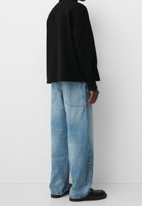 Svart, oversized jacka med en jämn textur, kombinerad med ljusblå vida jeans med subtila blekningar och sydda detaljer, samt svarta skor.