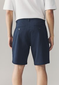 Tumesinised lühikesed püksid on tehtud siledast puuvillast kangast, kahe tagatasku ja nupu kinnitustega, sirge äärega. Pole nähtavaid mustreid ega kaunistusi.