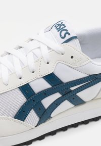 White sneaker featuring blue leather accents, mesh panels, and white laces. Textured sole for grip, with "asics" logo on the tongue.