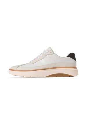 Vit lädersneaker med en krämfärgad gummisula, bruna accenter, runda snörningar och en svart hälplatta, med en slät och texturerad finish.