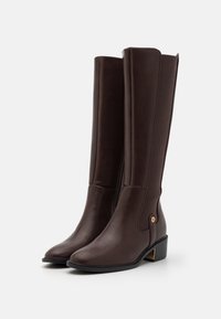Bottes hautes marron en cuir lisse avec un embout arrondi, une fermeture éclair latérale, un panneau élastique et un petit talon orné d'un accent doré.