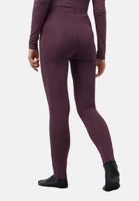 Leggings aderenti di un profondo bordeaux, con una texture a coste e una vita alta. La modella è in piedi con calzini neri, mostrando la vista laterale.