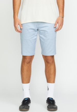 Light blue shorts with a smooth texture, knee-length fit, and elastic waistband, paired with black sneakers and white socks.