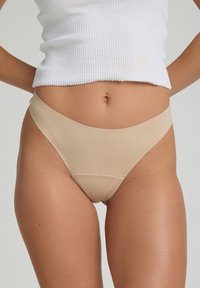 Culottes de bikini beiges sans couture avec une texture lisse et des ouvertures de jambe échancrées. Associées à un haut blanc à rayures, affichant un design minimaliste.