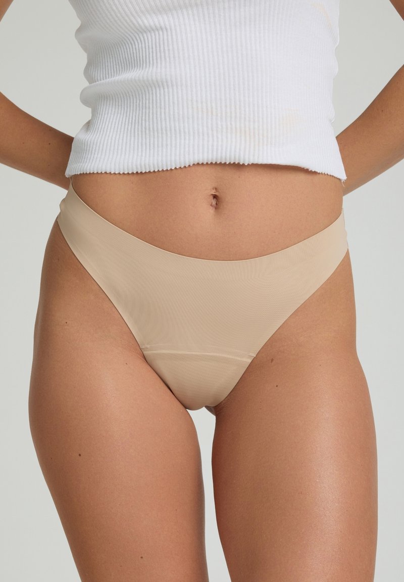 Culottes de bikini beiges sans couture avec une texture lisse et des ouvertures de jambe échancrées. Associées à un haut blanc à rayures, affichant un design minimaliste.