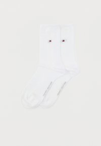 Άσπρες βαμβακερές κάλτσες με υφασμένες κατακόρυφες ρίγες, διαθέτοντας ένα μικρό λογότυπο σε κόκκινο, άσπρο και μπλε. Ενισχυμένη φτέρνα και μύτη, με το εμπορικό σήμα "TOMMY HILFIGER".