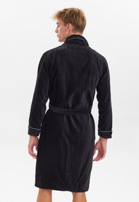 Accappatoio di spugna nero con maniche lunghe, cintura coordinata e bordo bianco sui polsini, dotato di colletto e lunghezza fino al polpaccio.