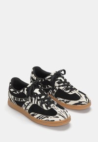 Sorte og hvide sneakers med zebra-mønster, lavet af ruskind og stofmaterialer, sorte snørebånd og en gummisål. Lav profil design.