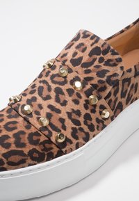 Sneaker im Leopardenmuster mit strukturierter Oberfläche, goldenen Nieten und weißer Gummisohle. Verfügt über ein Slip-On-Design ohne sichtbare Schnürsenkel.