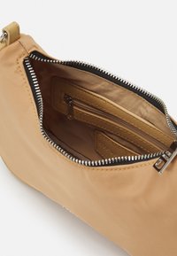 Borsa a tracolla in nylon beige con chiusura a zip, tasca interna e dettagli in metallo dorato. Texture liscia con dettagli di design minimalisti.