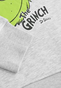 Sweatshirt gris avec le personnage du Grinch en vert vif et texte noir. Poignets côtelés et texture de tissu lisse. Marque Dr. Seuss.