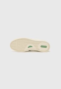 Schuhsohle mit einem strukturierten Gummimuster, das einen grünen Akzent und eine cremefarbene Basis aufweist, entworfen für Traktion und Haltbarkeit.