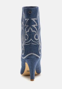 Denimist ankle boot kitsasis, sinine kangas, ja hõbedane dekoratiivne õmblus. Ümar varvas ja bränditud kuldne aktsent üleval.
