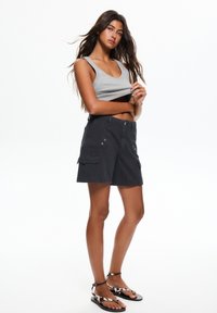 Top grigio senza maniche abbinato a pantaloni cargo scuri con tasche frontali, chiusura con bottone e accessori decorativi. Sandali in bianco e nero.