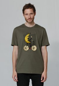 Olivegrünes Baumwoll-T-Shirt mit einem grafischen Design eines Bananen, die ein Fahrrad fährt, in kräftigen Farben und verspielten Details.