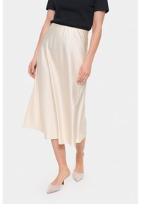 Satin midi suknja u boji off-white, s glatkom teksturom i lepršavim siluetom. Uparena s svijetlim ukrašenim štiklama.