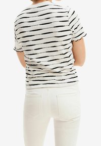 Czarna i biała pasiasta dzianinowa bluzka z krótkimi rękawami i falistymi brzegami, zestawiona z białymi dopasowanymi spodniami.