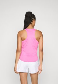 Fitted pink athletic tank top with a racerback design, featuring a smooth texture and minimal white branding on the back. Worn with white shorts.