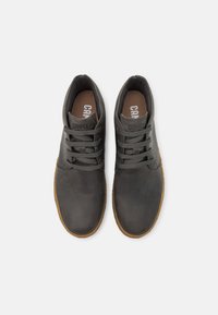 Zapatillas de cuero gris oscuro con puntera redonda, suelas marrones y cierre con cordones. Marca "Camper" destacada en la lengüeta y en la plantilla.