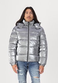 Giacca puffa argento metallico con collo alto, chiusura a zip e cappuccio removibile. Presenta polsini a coste e design trapuntato.