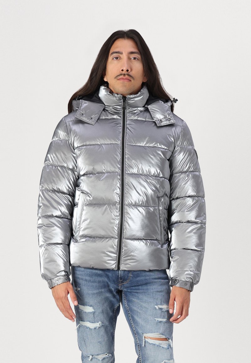 Giacca puffa argento metallico con collo alto, chiusura a zip e cappuccio removibile. Presenta polsini a coste e design trapuntato.