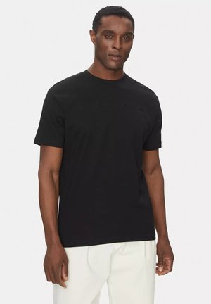 T-shirt nero a maniche corte in cotone con colletto a girocollo. Presenta testo in rilievo sul petto. Texture liscia, design semplice.