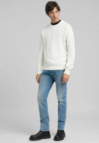 Maglione bianco a coste abbinato a jeans di denim azzurro chiaro e stivaletti neri chunky. Design semplice, tessuto testurizzato e vestibilità casual.