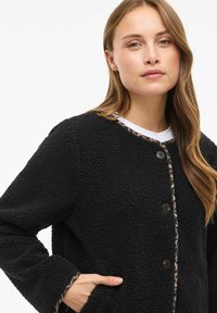 Giacca in pile nera con superficie testurizzata, bordo a stampa leopardata e chiusura con bottoni. Presenta tasche frontali e scollatura rotonda.