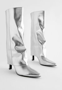 Bottines en métal argenté avec un design décontracté, bouts pointus et talons aiguilles de 3 pouces. Texture lisse et détails de couture sans couture.