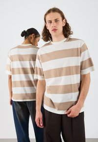 Short-sleeve, crew-neck T-shirt featuring wide horizontal stripes in beige and off-white. Fabric appears soft with a relaxed fit.