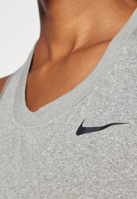 Szary sportowy top bez rękawów wykonany z teksturowanej tkaniny, z czarnym logo Nike na lewej stronie klatki piersiowej oraz żebrowanym dekoltem.