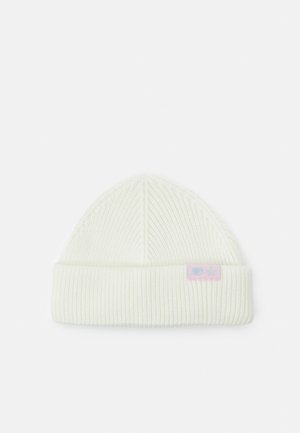 Bonnet en tricot blanc avec texture côtelée, présentant un revers et une petite étiquette rose affichant un motif d'étoiles. Convient à différentes tailles de tête.