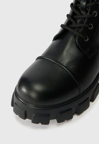 Μαύρη δερμάτινη μπότες μέχρι τον αστράγαλο με στρογγυλή μύτη, υφαμένη επιφάνεια και χοντρή λάστιχη σόλα με βαθιές αυλακώσεις για πρόσφυση. Χωρίς κορδόνια.